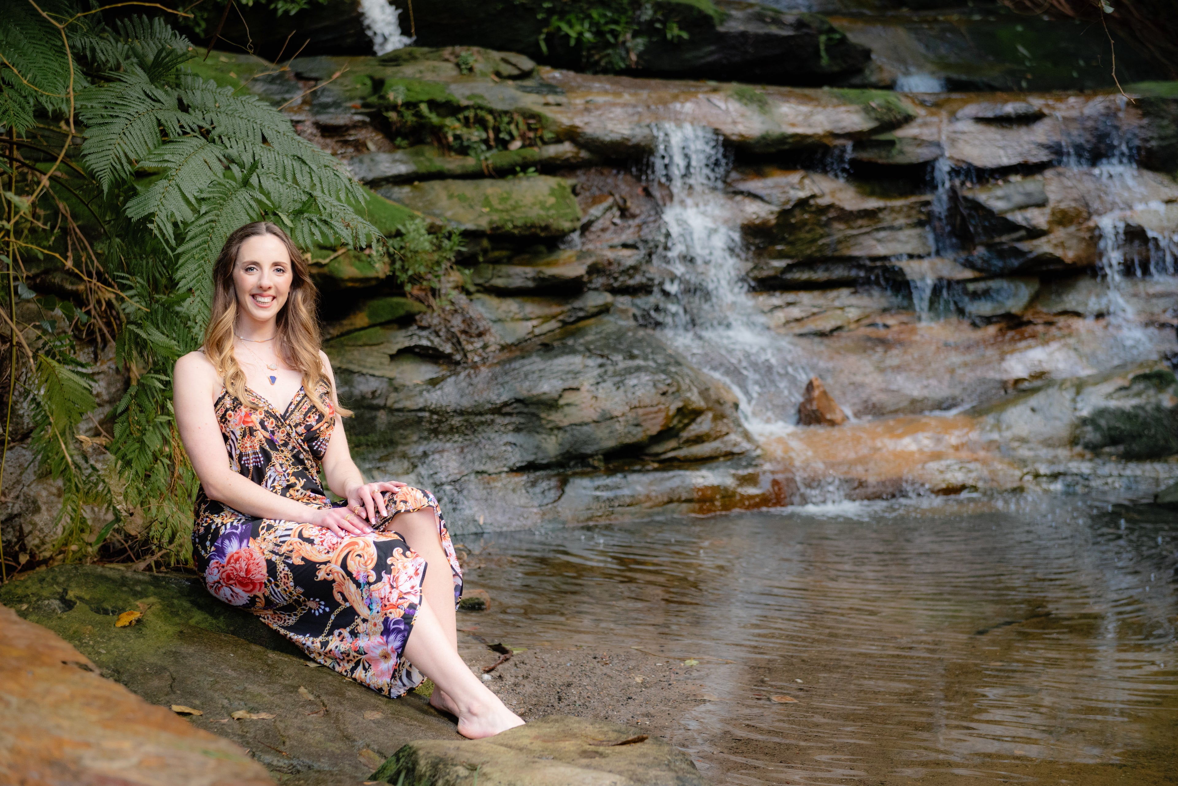 Woman in a floral dress sitting by a waterfall in a natural setting